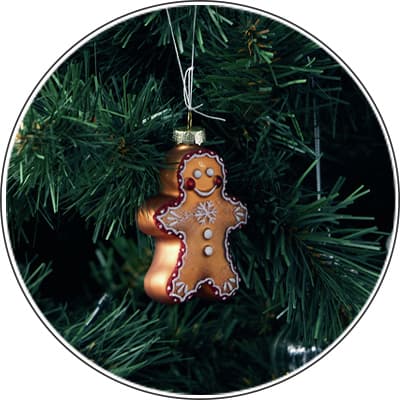 Lebkuchenmann-Anhänger hängt an einem grünen Weihnachtsbaum, dekoriert mit Zuckerguss-Verzierungen und einem Schneeflockenmuster