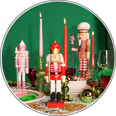 Drei Nussknackerfiguren in Weihnachtsdeko auf grünem Hintergrund, umgeben von Kerzen, Gläsern und Kugeln auf einem Tisch