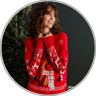 Frau in rotem Weihnachts-Pullover mit Rentier-Motiv steht vor einem Tannenbaum