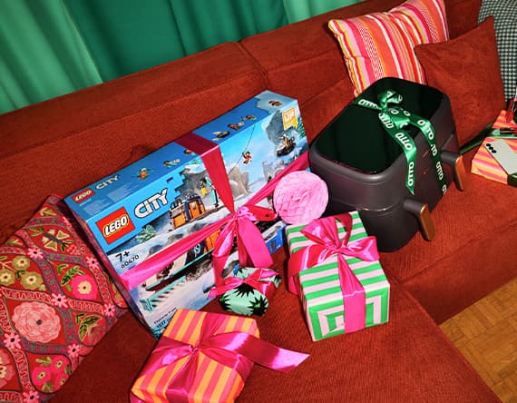 Geschenke auf rotem Sofa – LEGO City Set, schwarzer Koffer, und bunt verpackte Geschenke mit Schleifen