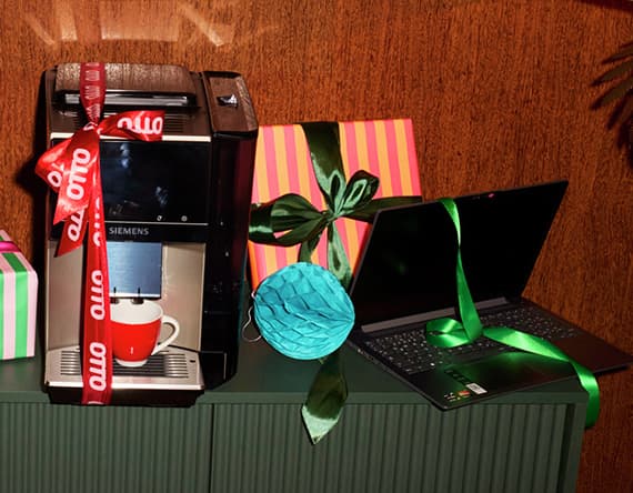 Otto – Kaffeemaschine mit roter Tasse und Laptop, beide mit Schleifen dekoriert, vor bunten Geschenkboxen