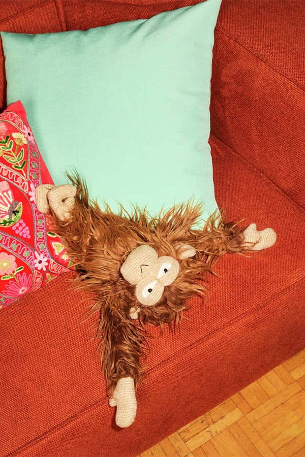 Plüschaffe liegt auf orangefarbenem Sofa neben türkisfarbenem und bunt besticktem Kissen