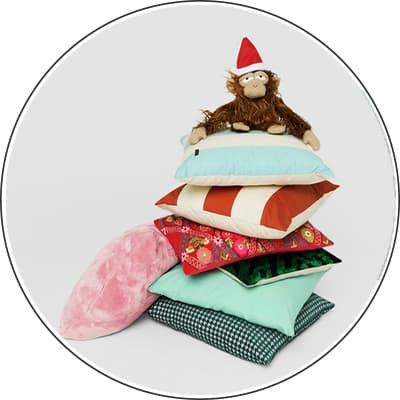 Verschiedene farbige Kissen gestapelt, oben sitzt ein Plüschtier-Affe mit roter Weihnachtsmütze