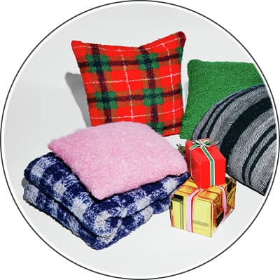 Zwei bunte Kissen, zwei gefaltete Decken und drei kleine Geschenke mit Schleifen auf weißem Hintergrund