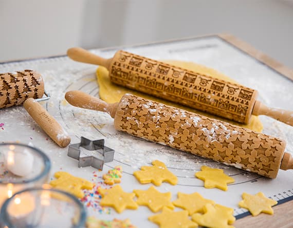 Teigrollen mit Mustern und ausgestochene Sternkekse auf bemehltem Tisch mit Kerzen und Streuseln