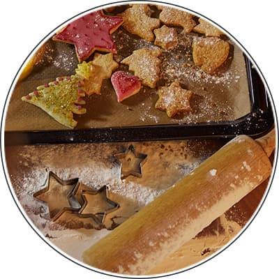 Plätzchen in verschiedenen Formen auf einem Backblech und Teig mit Stern-Ausstechformen und einem Nudelholz auf bemehlter Fläche