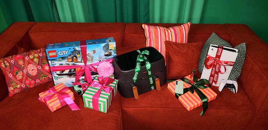 Geschenkideen – LEGO City Set, schwarze Tasche, verpackte Geschenke, Smartphone, alles auf rotem Sofa mit grünen Kissen
