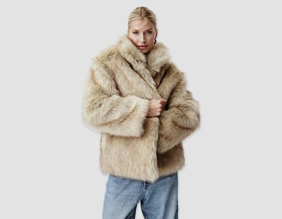 Person trägt beige Kunstpelzjacke und blaue Jeans, Gesicht ist verschwommen