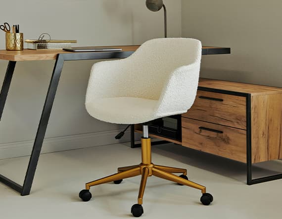 Moderner Schreibtischstuhl vor Holz-Schreibtisch mit Schubladen und Metallbeinen, daneben Tischlampe und Bürobedarf