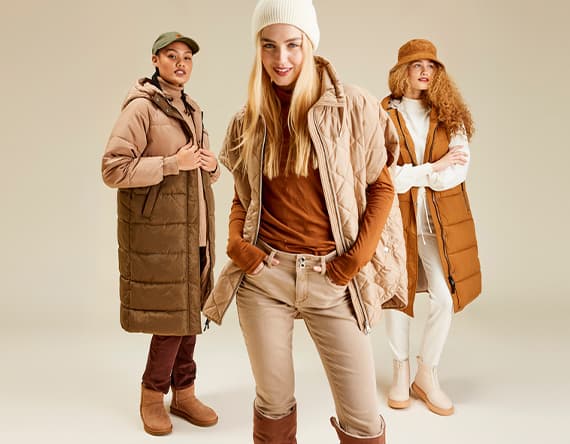 Drei Personen in beige und braunen Winteroutfits, stehend vor neutralem Hintergrund