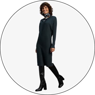 Frau in dunkelgrünem, langärmeligen Kleid und schwarzen Stiefeln mit Absatz steht seitlich und trägt ein gemustertes Halstuch