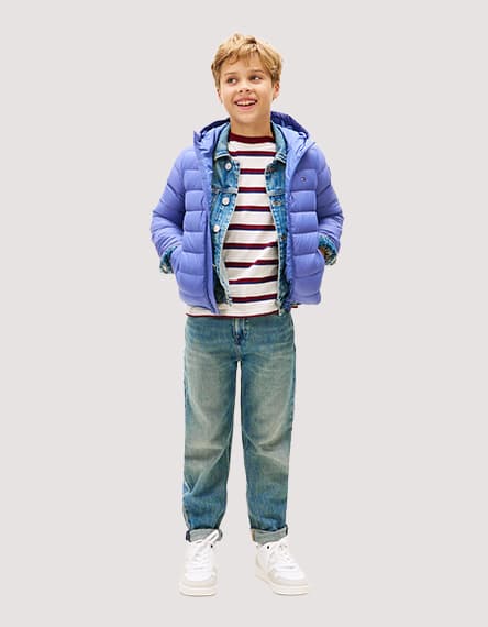 Junge trägt blauen Daunenmantel, gestreiftes Shirt, Jeansjacke, blaue Jeans und weiße Turnschuhe.