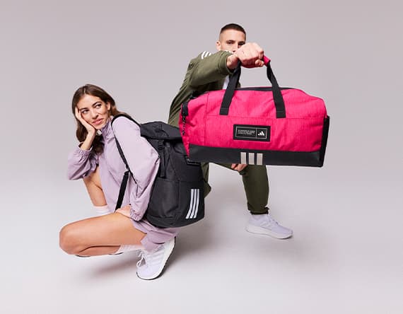 Person mit schwarzem Rucksack und Person mit roter Sporttasche posieren vor grauem Hintergrund.