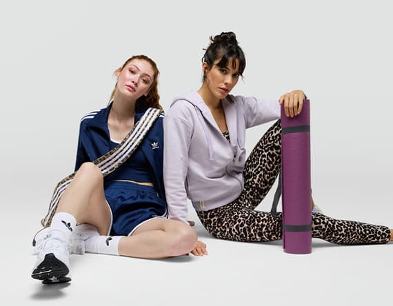 Zwei Frauen in Sportkleidung, eine hält eine Yogamatte, die andere trägt ein blaues Adidas-Outfit.