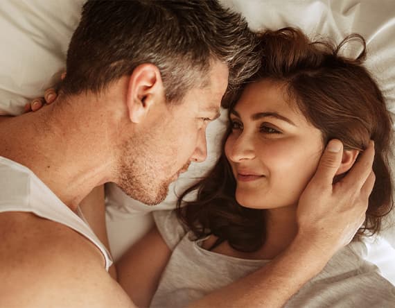 Zwei Personen liegen nah beieinander im Bett, eine Person hält die andere sanft am Kopf.