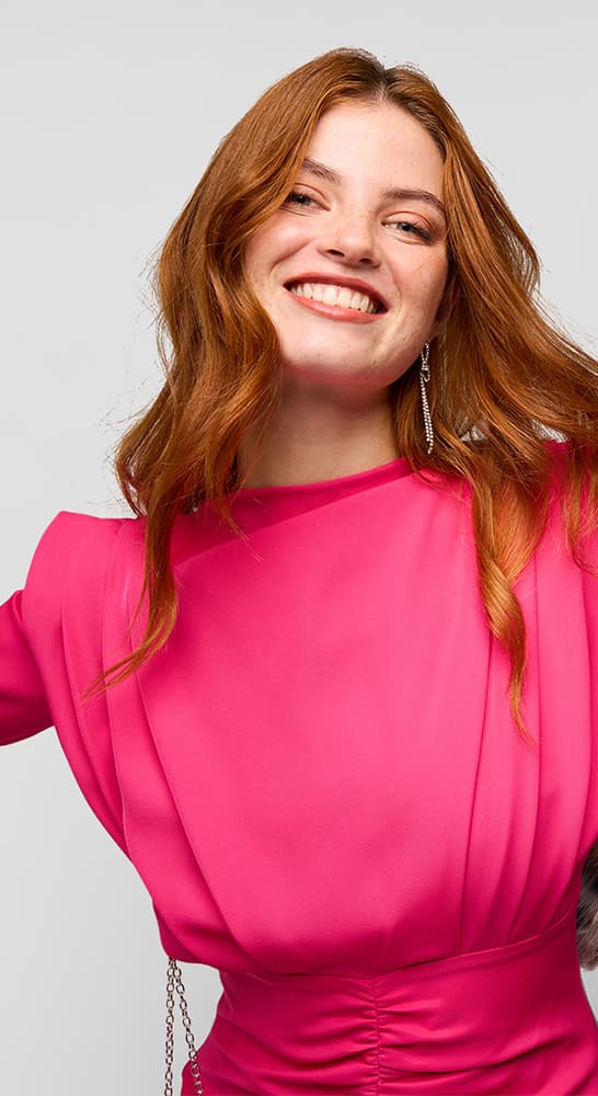 Frau mit roten Haaren trägt ein pinkes Kleid mit langen Ärmeln.