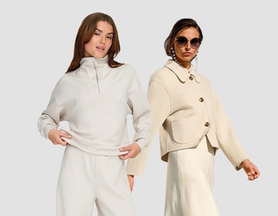 Zwei Frauen in beigefarbener Kleidung, eine im Hoodie und weiten Hosen, die andere im Mantel und Rock, tragen eine Tasche.