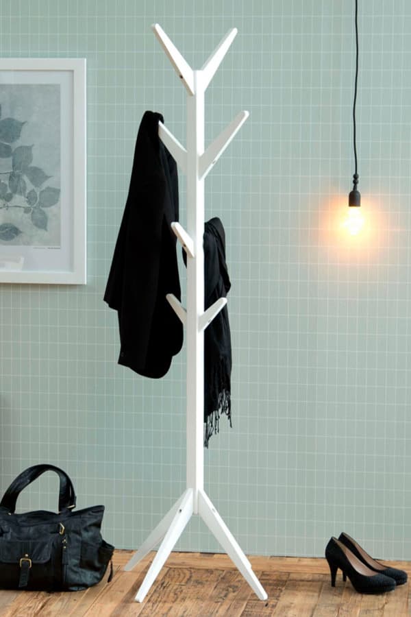 Weißer Garderobenständer mit schwarzem Mantel und Schal, daneben schwarze Tasche und Schuhe auf Holzboden.