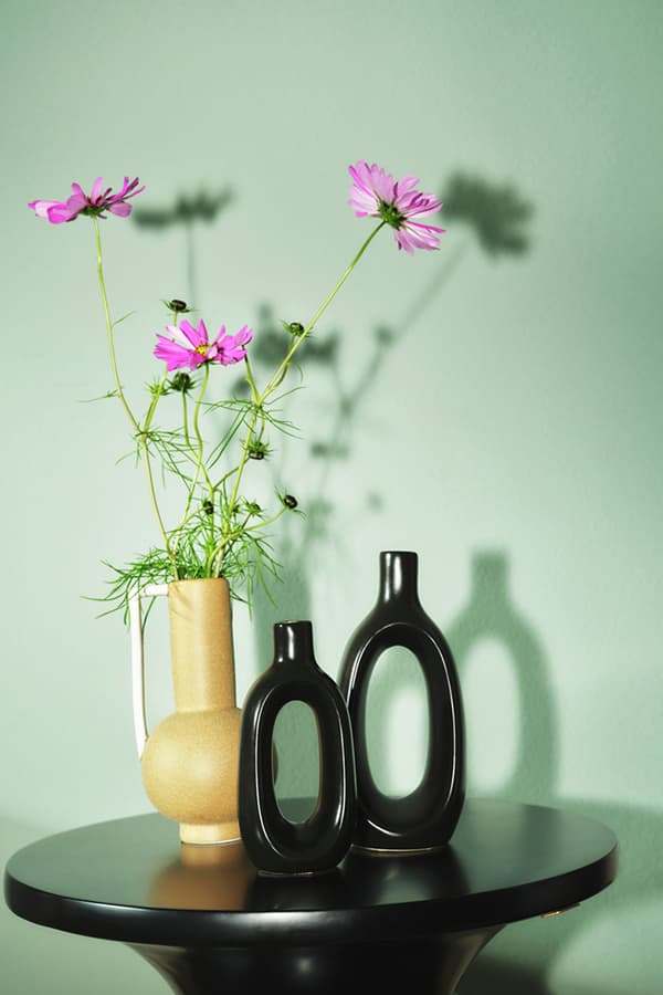 Holzkommode mit zwei Lampen, Büchern und einem abstrakten Bild an der rosa Wand