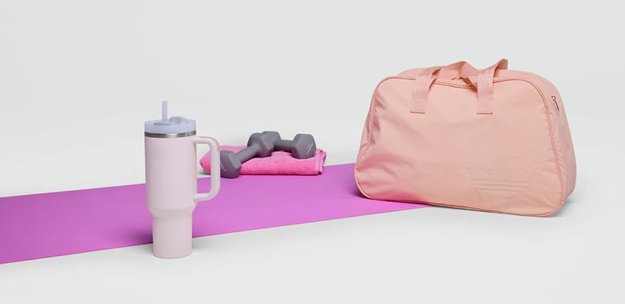 Sporttasche, Hantel, Handtuch und Trinkbecher auf einer pinken Yogamatte.