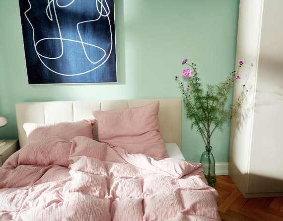 Bett mit rosa Bettwäsche, grüne Wand, abstrakte Kunst und Vase mit Blumen daneben