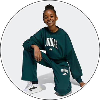 Person in grünem Adidas-Sweatshirt und -Jogginghose, kniet auf einem Bein, trägt weiße Sneakers