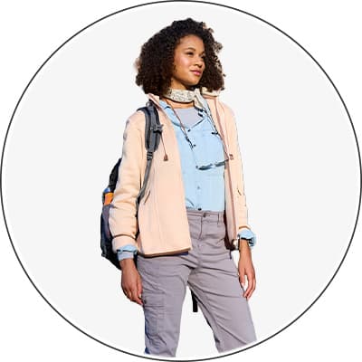 Frau in Outdoor-Kleidung mit Rucksack, helle Jacke und graue Hose, steht aufrecht