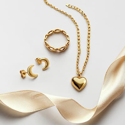 Goldene Herz-Halskette, Ring mit Kettengliedern, Mond-Ohrringe und cremefarbenes Band auf hellem Hintergrund.