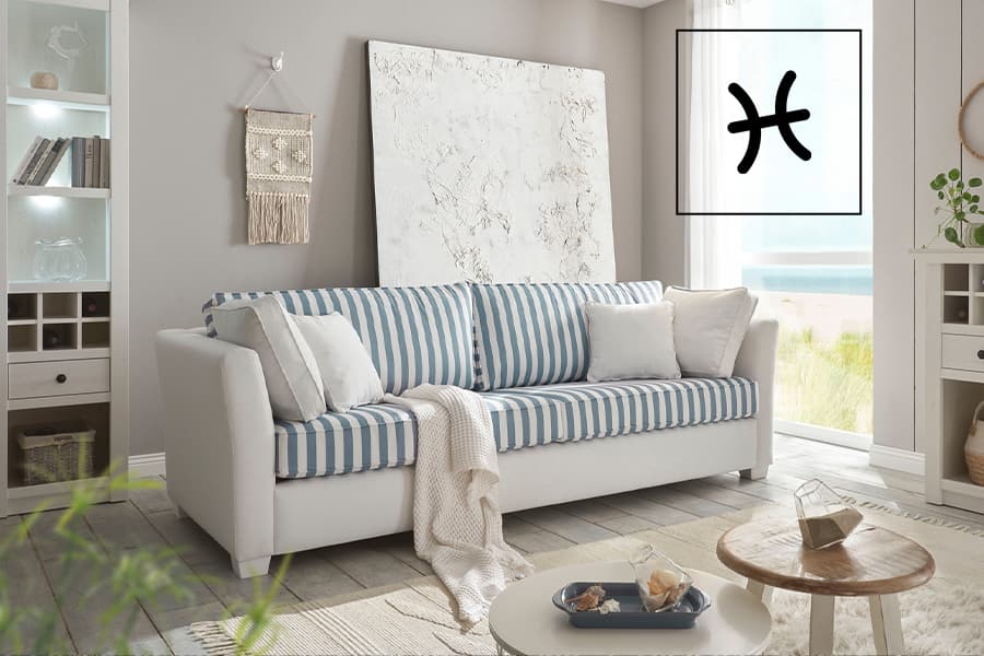 Gemütliches Wohnzimmer mit weiß-blau gestreiftem Sofa, Wanddeko und großem Fenster mit Meerblick.