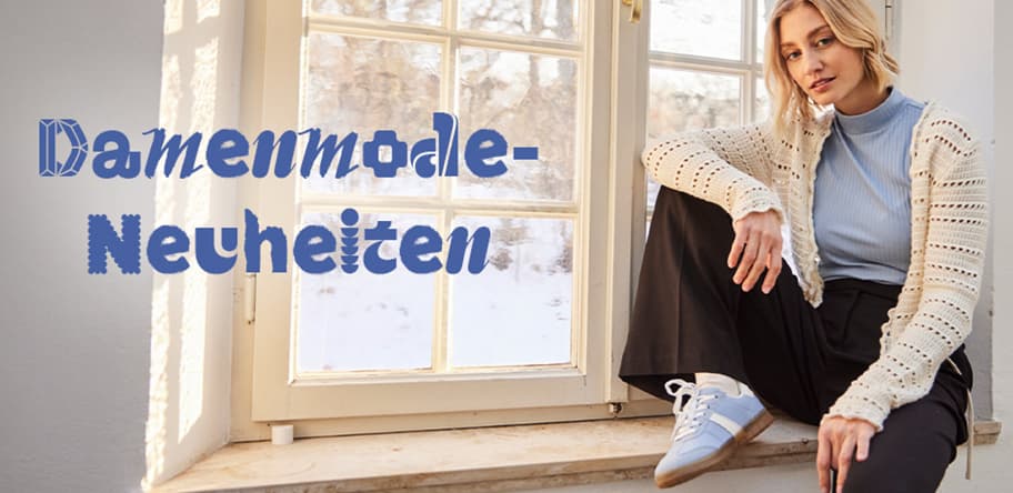 Damenmode-Neuheiten – Frau in hellblauem Oberteil und gestrickter Jacke sitzt lässig auf Fensterbank.