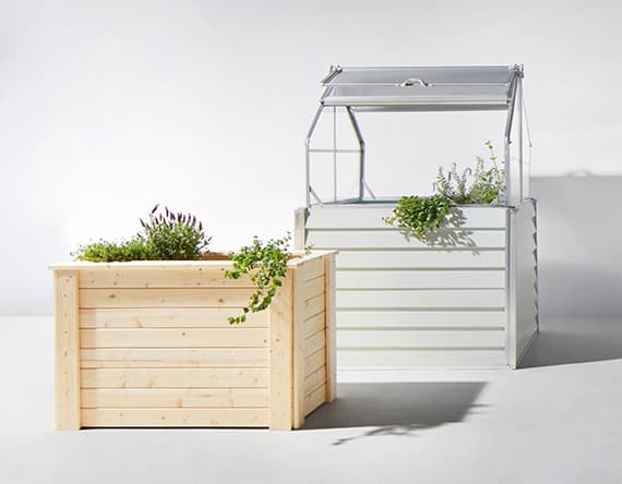 Zwei Hochbeete, eins aus Holz und eins mit Überdachung, bepflanzt mit Kräutern und Blumen.