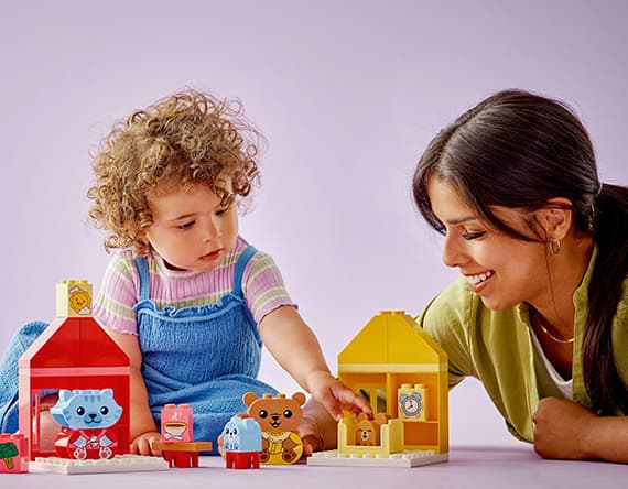 Kind und Erwachsene spielen gemeinsam mit bunten Spielzeughäusern und Figuren.