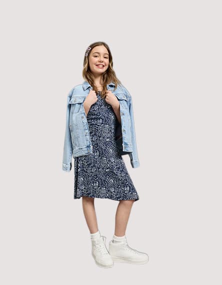 Mädchen in dunkelblauem Kleid mit Schmetterlingsmuster und weißem Gürtel, trägt rosa Ballerinas.