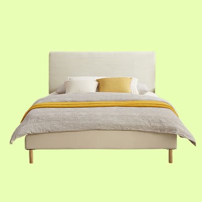 Modernes Bett mit weißem Kopfteil, grauer Bettdecke und gelbem Akzentkissen auf hellgrünem Hintergrund.