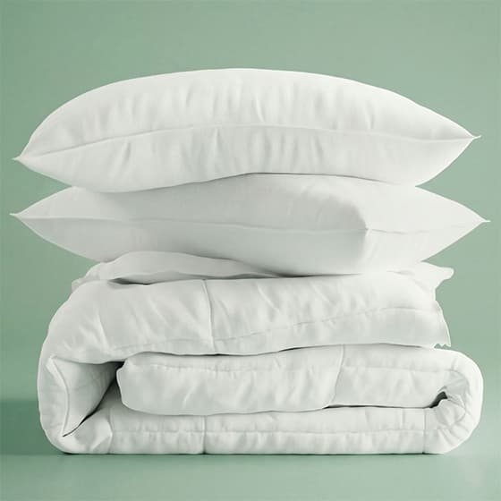 Gestapelte weiße Kissen und Bettdecke vor grünem Hintergrund.