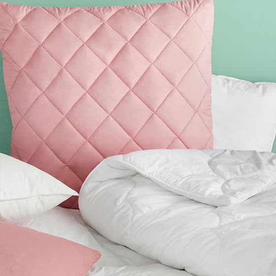 Rosa gesteppter Kissenbezug, umgeben von weißen Bettdecken und Kissen.