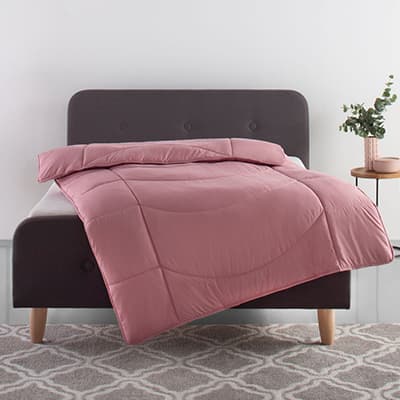 Rosa Bettdecke auf grauem Bett, daneben ein Nachttisch mit Pflanze