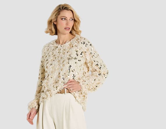 Frau trägt cremefarbenen Pullover mit Strukturmuster und weiße Hose.