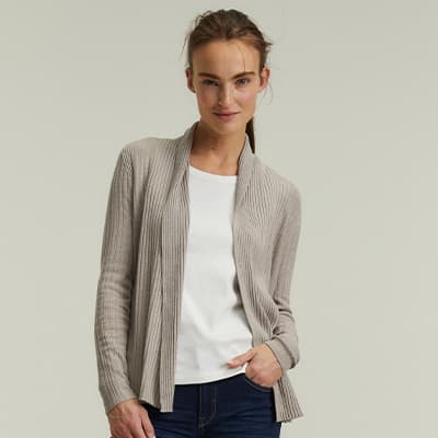 Frau trägt eine beige Strickjacke über einem weißen T-Shirt und dunklen Jeans, eine Hand in der Tasche.