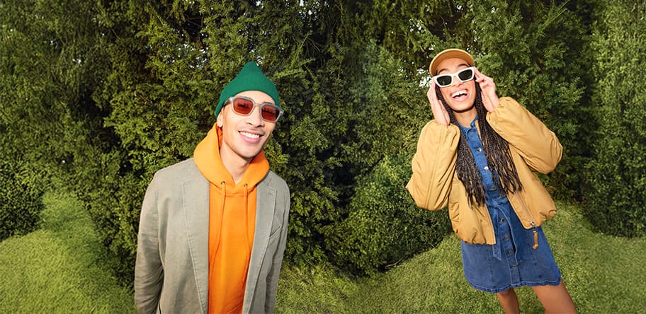 Zwei Personen posieren im Garten, links im Hoodie mit Jacke, rechts im Jeanskleid mit weiter Jacke und Mütze