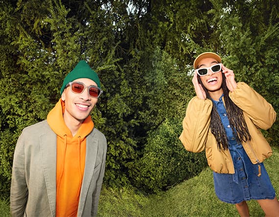 Zwei Personen posieren im Grünen, links mit Kapuzenpulli und Jacke, rechts mit Kleid und kurzer Jacke