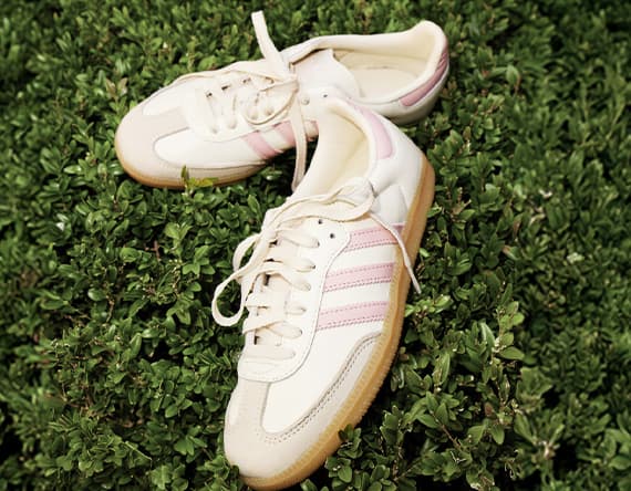 Beige Sneaker mit rosa Streifen liegen locker auf dichtem grünen Busch