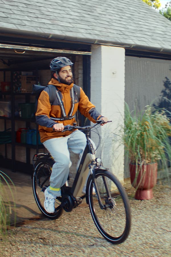 Person mit Helm fährt auf einem E-Bike aus einer offenen Garage auf einen Kiesweg