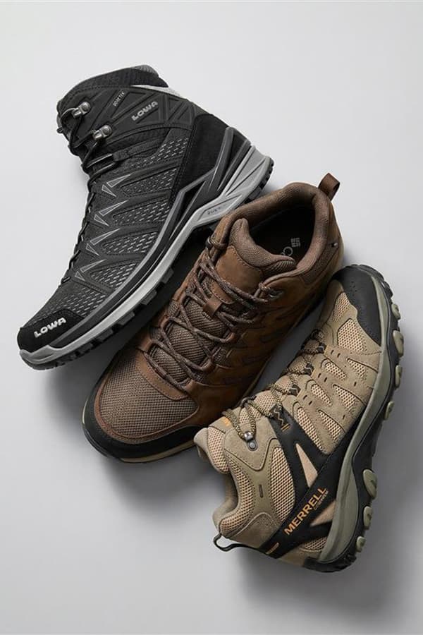 Drei Wanderhalbschuhe in Schwarz, Braun und Beige liegen versetzt nebeneinander auf hellem Hintergrund
