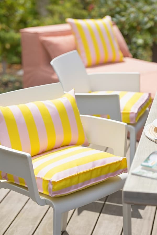 Weiße Gartenstühle mit gelb-rosa gestreiften Sitz- und Rückenkissen neben Tisch und Liege auf Holzterrasse