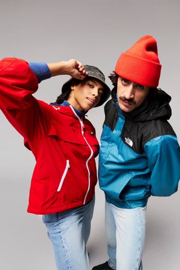 Zwei Personen in roten und blau-schwarzen Outdoorjacken stehen nah beieinander und tragen helle Jeans