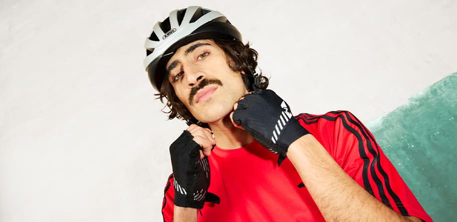 Person im roten Sportshirt mit Fahrradhelm und fingerlosen Handschuhen hält die Hände vor das Gesicht