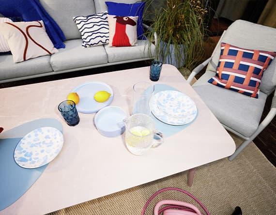 Terrassentisch mit bunten Tellern, Gläsern und Karaffe mit Zitronen, dahinter Sofa und Sessel mit gemusterten Kissen