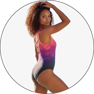 Frau im einteiligen Badeanzug mit pink-lila Farbverlauf, seitlich stehend, eine Hand im lockigen Haar