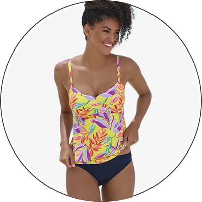 Frau in buntem Tankini-Oberteil mit Blattmuster und dunkelblauer Bikinihose steht vor hellem Hintergrund